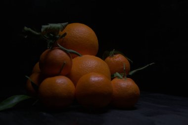 Portakallar ve mandalinalar siyah bir yüzeye dizilmiş.