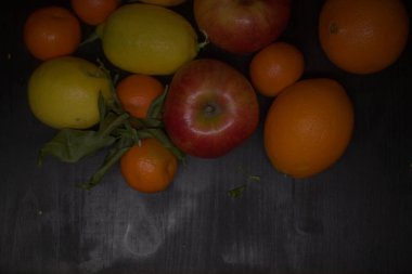 Siyah bir yüzey üzerinde limon ve portakallı mandalina ve elmalar