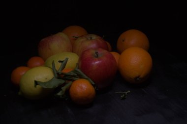 Siyah bir yüzey üzerinde limon ve portakallı mandalina ve elmalar