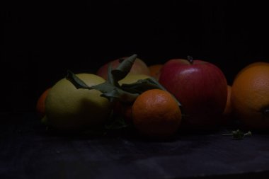 Siyah bir yüzey üzerinde limon ve portakallı mandalina ve elmalar