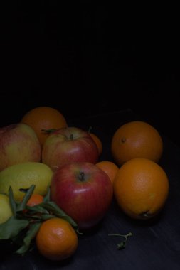 Siyah bir yüzey üzerinde limon ve portakallı mandalina ve elmalar