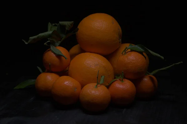 橘子和橘子堆积在一个黑色的表面上 — 图库照片