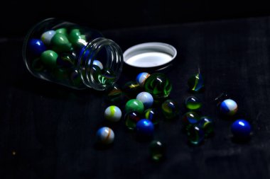 Siyah bir yüzey üzerinde renkli misketlerle dolu kavanoz.