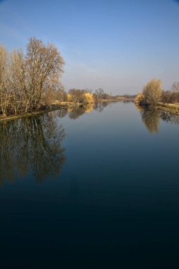 Yansımaları İtalya kırsalında suya dökülen çıplak ağaçlarla çevrili bir nehir.