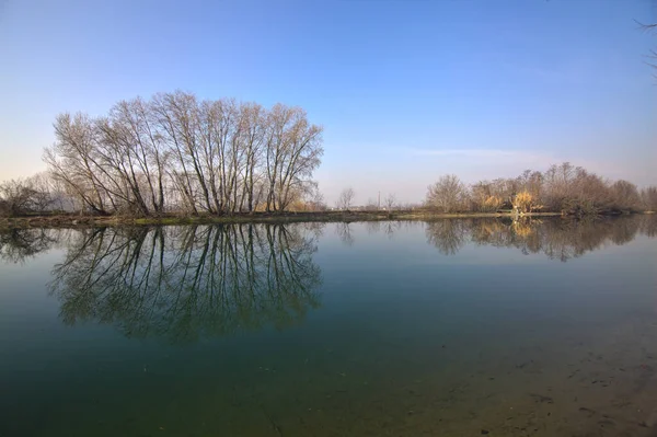川はイタリアの田舎で水に投げられた反射と裸の木に囲まれています — ストック写真