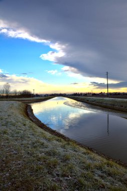 Kışın bir patikanın yanındaki su deresi. İtalya 'nın kırsal kesimlerinde gökyüzü suya dökülüyor.