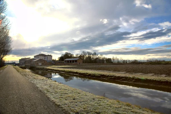 冬の道の隣の水の流れ イタリアの田舎の水に投げられた空 — ストック写真