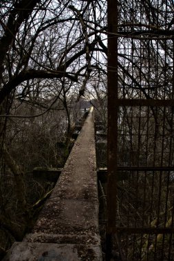 İtalya kırsalındaki bir nehre giden çıplak ağaçlarla dolu bir parkın üzerindeki beton köprü.