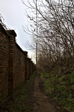 Tuğla bir sınır duvarı ve italyan kırsalında bir set ile çevrili çamurlu bir yol.
