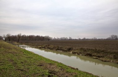 İtalya 'nın kışın kırsalında çıplak ağaçlarla çevrili bir tarlanın yanındaki su akıntısı.