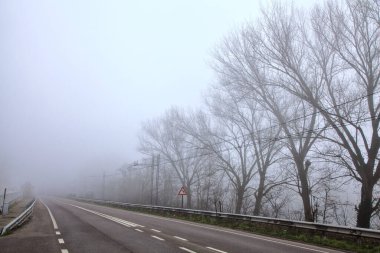 İtalya kırsalında sisli bir günde, ucunda demiryolu olan bir yol.