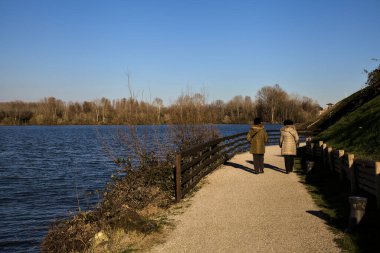 Kışın gün batımında gölün kıyısında yürüyen iki kadın.