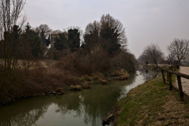 İtalya 'nın kırsal kesimlerinde, bulutlu bir günde, kenarlarında çıplak ağaçlar olan su akıntısı.