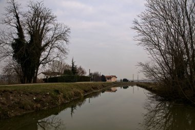 İtalya 'nın kırsal kesimlerinde, bulutlu bir günde, kenarlarında çıplak ağaçlar olan su akıntısı.
