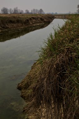 Kışın bulutlu bir günde İtalya kırsalındaki tarlaların yanındaki su akıntısı