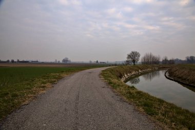 Kışın İtalya 'nın kırsal kesimlerinde su ve tarlaların yanında bisiklet yolu.