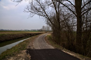 Kışın İtalya 'nın kırsal kesimlerinde su ve tarlaların yanında bisiklet yolu.