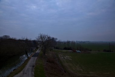 İtalya 'nın kırsal kesimlerinde, bulutlu bir günde, kenarlarında çıplak ağaçlar olan su akıntısı.