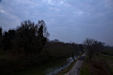 İtalya 'nın kırsal kesimlerinde, bulutlu bir günde, kenarlarında çıplak ağaçlar olan su akıntısı.