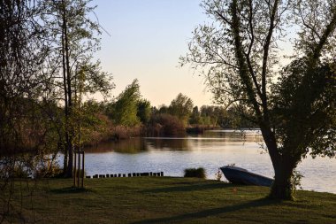 Gün batımında bir gölün kıyısında, bir tekne karaya oturmuş.