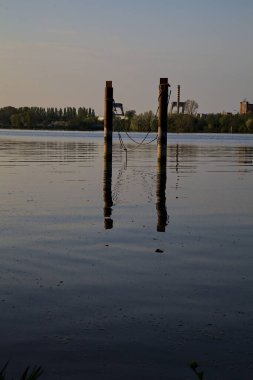 Gölde demirleyen direkler, yansımaları suya dökülür.