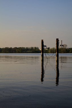Gölde demirleyen direkler, yansımaları suya dökülür.