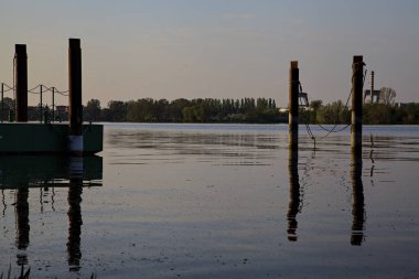 Gölde demirleyen direkler, yansımaları suya dökülür.