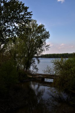 İlkbaharda İtalya kırsalında bir köprüsü olan parktaki bir nehrin körfezi