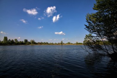 Gölgedeki bir nehrin kıyısında İlkbaharda İtalya kırsalındaki ağaçlar tarafından çerçevelenmiş