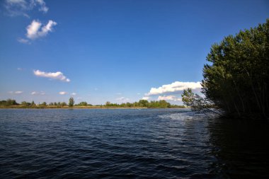 Gölgedeki bir nehrin kıyısında İlkbaharda İtalya kırsalındaki ağaçlar tarafından çerçevelenmiş