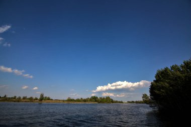 Gölgedeki bir nehrin kıyısında İlkbaharda İtalya kırsalındaki ağaçlar tarafından çerçevelenmiş