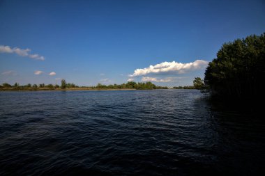 Gölgedeki bir nehrin kıyısında İlkbaharda İtalya kırsalındaki ağaçlar tarafından çerçevelenmiş