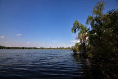 Gölgedeki bir nehrin kıyısında İlkbaharda İtalya kırsalındaki ağaçlar tarafından çerçevelenmiş