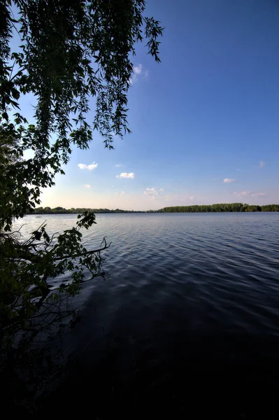 Gölgedeki bir nehrin kıyısında İlkbaharda İtalya kırsalındaki ağaçlar tarafından çerçevelenmiş