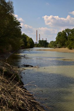 Uzakta bir elektrik santrali olan bir nehrin körfezi kıyılarda ağaçlarla çevrili.