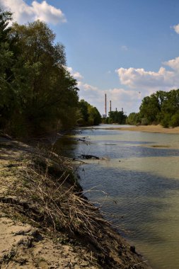 Uzakta bir elektrik santrali olan bir nehrin körfezi kıyılarda ağaçlarla çevrili.