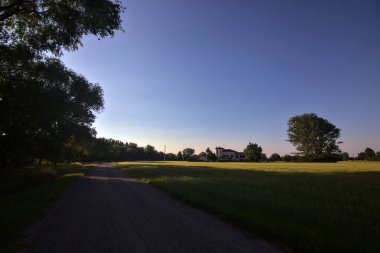 Gün batımında İtalya kırsalının gölgesinde bir tarla ile çevrili bir köy yolu.