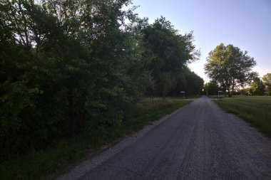 Gün batımında İtalya kırsalının gölgesinde bir tarla ile çevrili bir köy yolu.