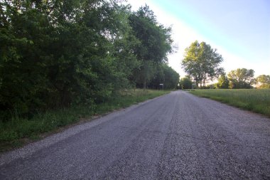 Gün batımında İtalya kırsalının gölgesinde bir tarla ile çevrili bir köy yolu.