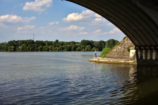 Fisherman on the shore of a lake under a bridge on a sunny day in summer