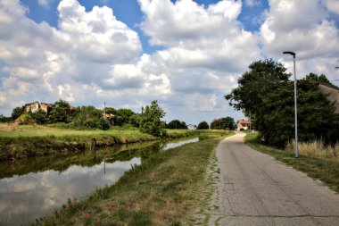 Yazın İtalya kırsalındaki bir köyün varoşlarındaki bir su deresinin yanında bisiklet yolu.