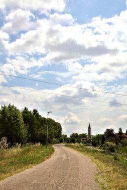 Yazın İtalya kırsalında bisiklet yolu. Uzakta çan kulesi var.