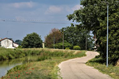 Yazın İtalya kırsalındaki bir köyün varoşlarındaki bir su deresinin yanında bisiklet yolu.