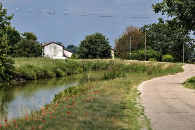 Yazın İtalya kırsalındaki bir köyün varoşlarındaki bir su deresinin yanında bisiklet yolu.