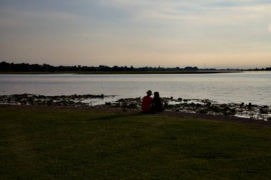 Yazın gün batımında gölün kıyısında oturan genç çift.
