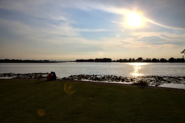 一对年轻夫妇坐在湖边 夕阳西下 — 图库照片