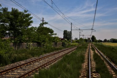 Yaz ortasında İtalya kırsalında, kenarlarında tarlalar olan demiryolu rayları.