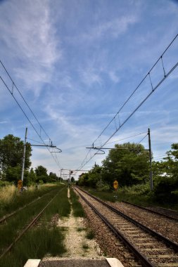 Yaz ortasında İtalya kırsalında boş bir istasyonun platformundan görülen raylar.