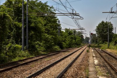 Yaz ortasında İtalya kırsalında boş bir istasyonun platformundan görülen raylar.