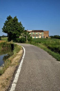 Tarlalı köy yolu ve yaz sonunda günbatımında terk edilmiş bir malikane.
